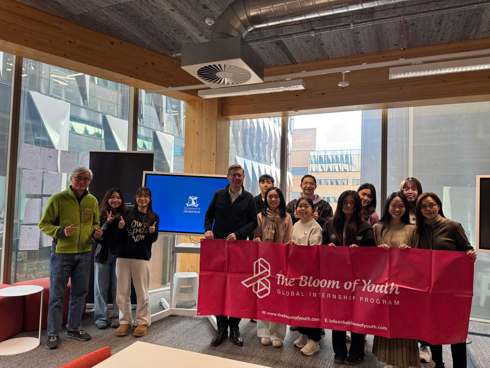 Bloom of Youth cohort holding the program banner with faculty at the University of Melbourne