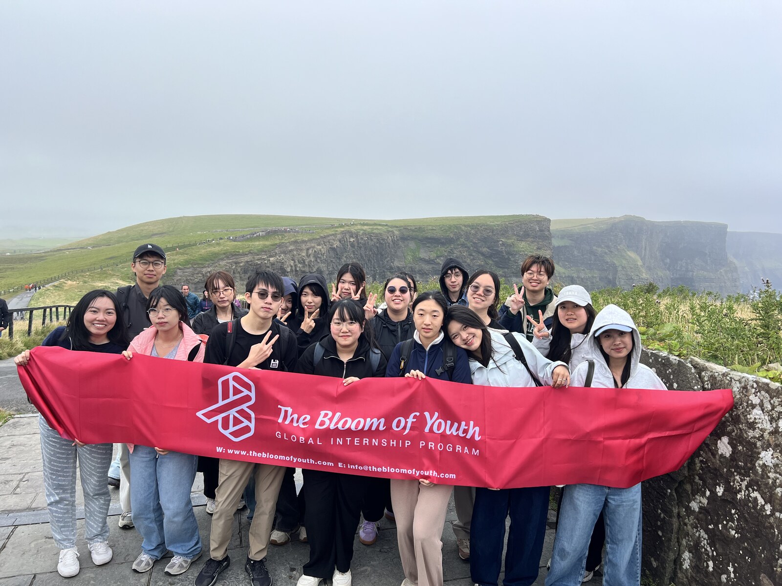 Bloom of Youth interns holding the Global Internship Program banner at the Cliffs of Moher, Ireland