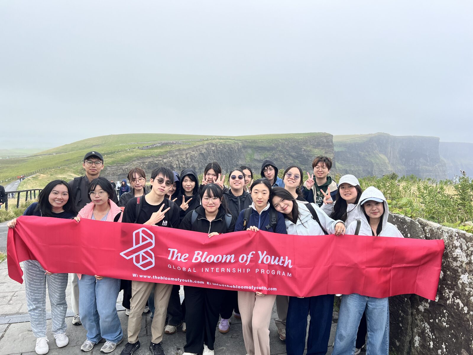 Bloom of Youth cohort holding the program banner at the Cliffs of Moher in Ireland