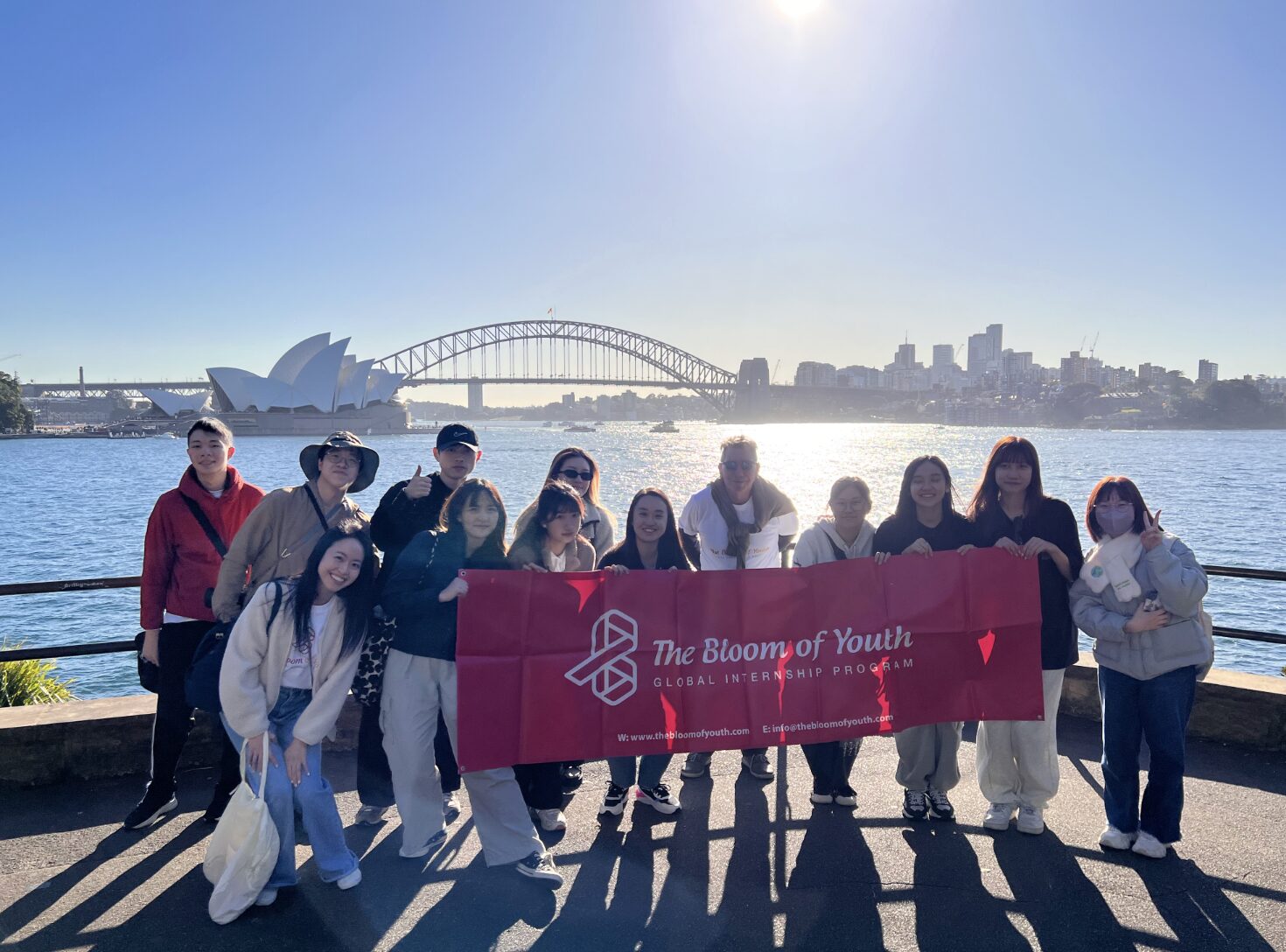 Bloom of Youth cohort with the program banner in front of Sydney Harbour Bridge and the Opera House